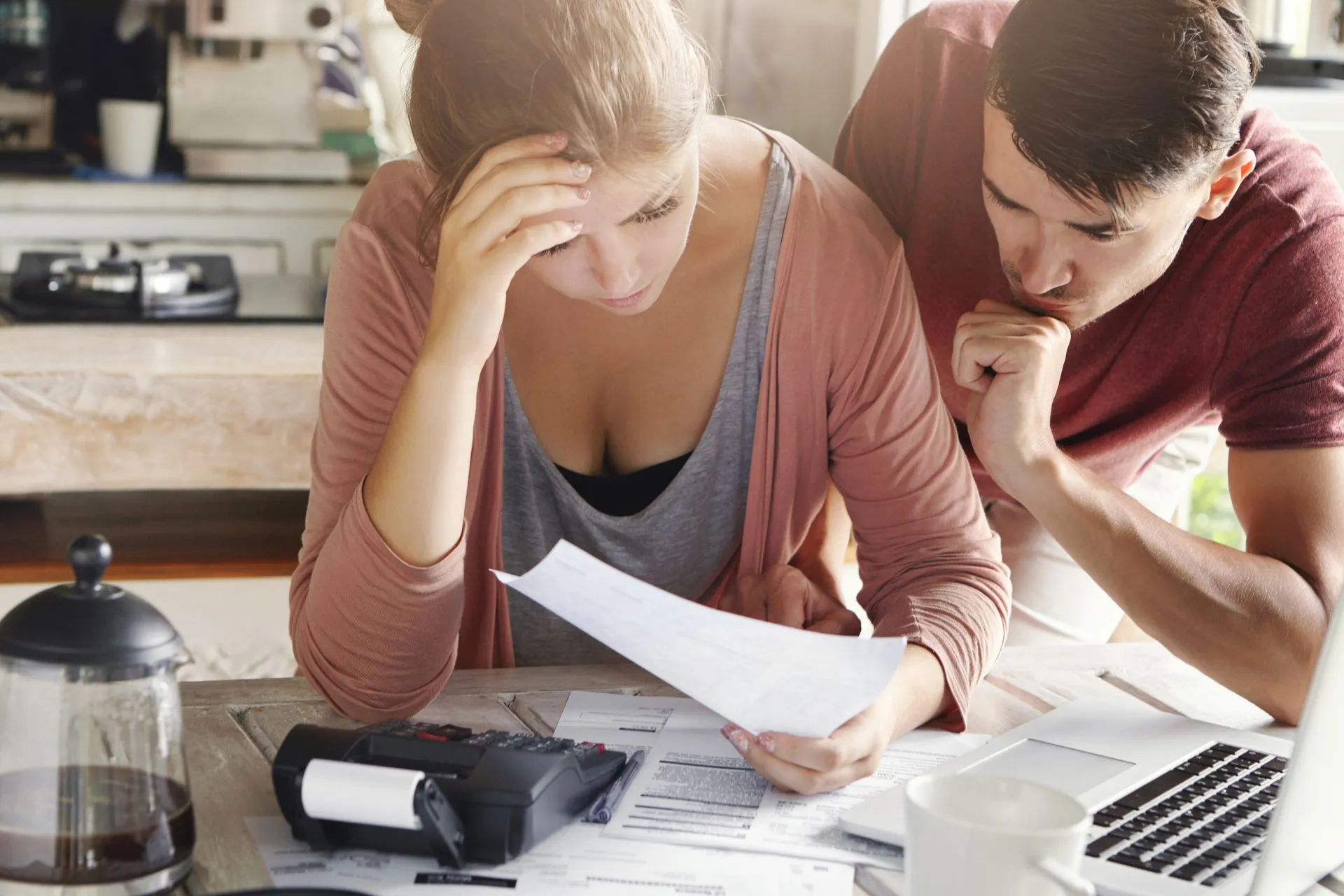 Un couple inquiet examinant des documents financiers et des factures sur une table avec une calculatrice et un ordinateur portable.